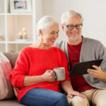 Älteres Ehepaar sitzt auf dem Sofa und informiert sich mit einem Tablet-PC